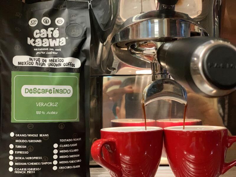 Espresso machine with 2 red mugs, a bag of Café Kaawa Descafeinado besides it