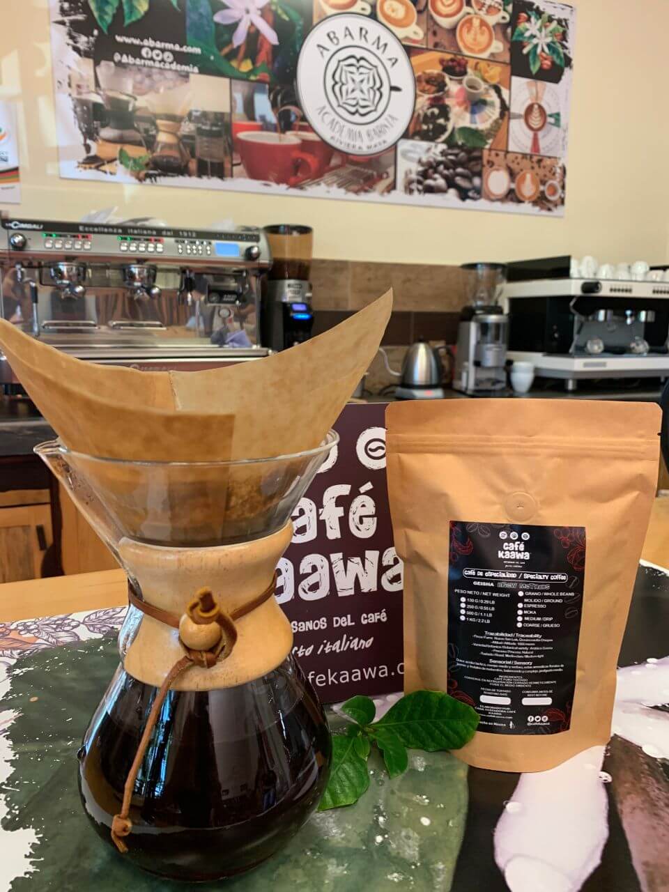 Coffee brewing in a pour over glass coffee pot besides a bag of specialty coffee geisha